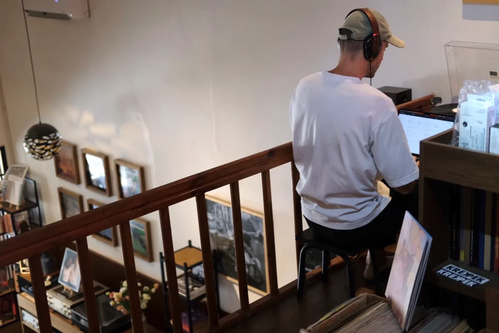 Levy sitting inside of a café, listening to an vinyl record why working on his laptop